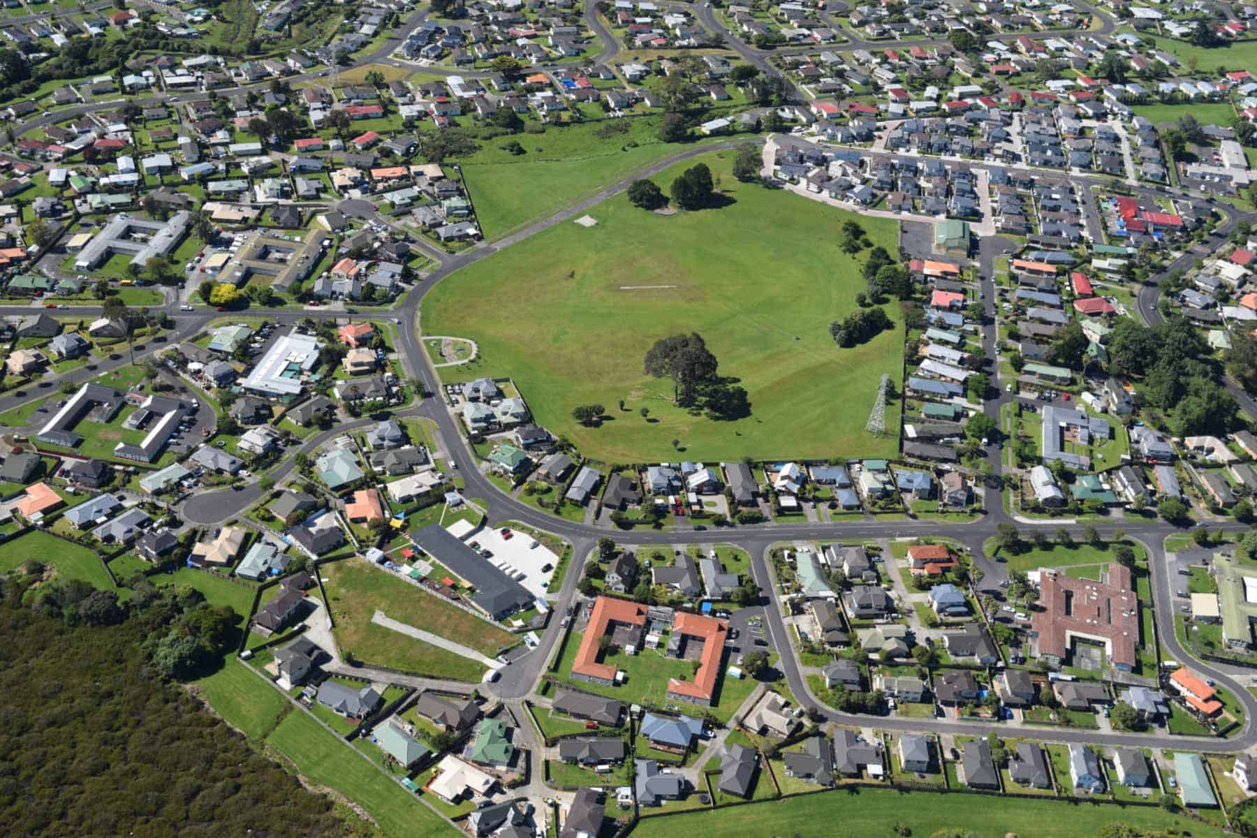 Aerial view of Boggust Park Crater, showing its grassy playing field, scattered trees and surrounding homes.