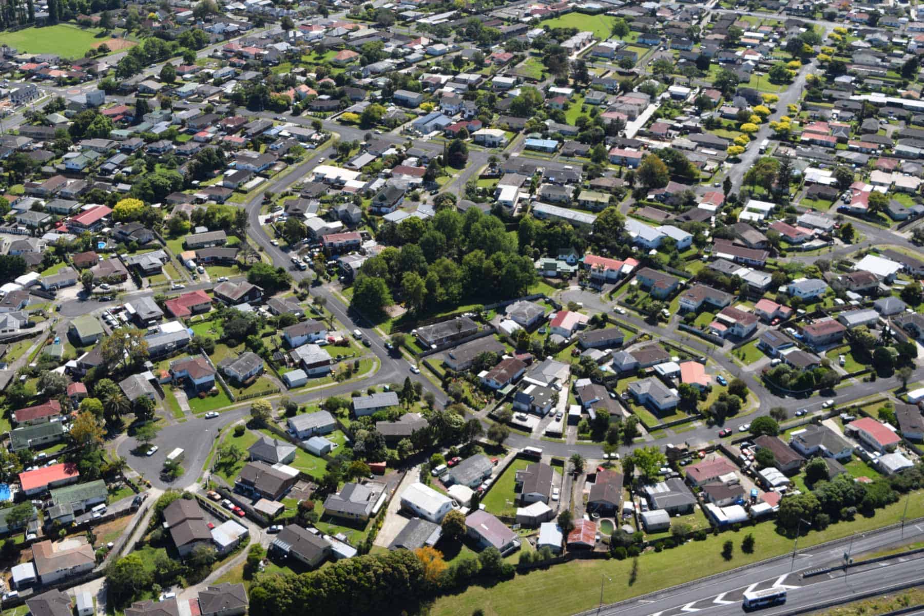 Aerial view of the residential area covering Cemetery Crater, with curving streets, houses and a wooded reserve beside the motorway.