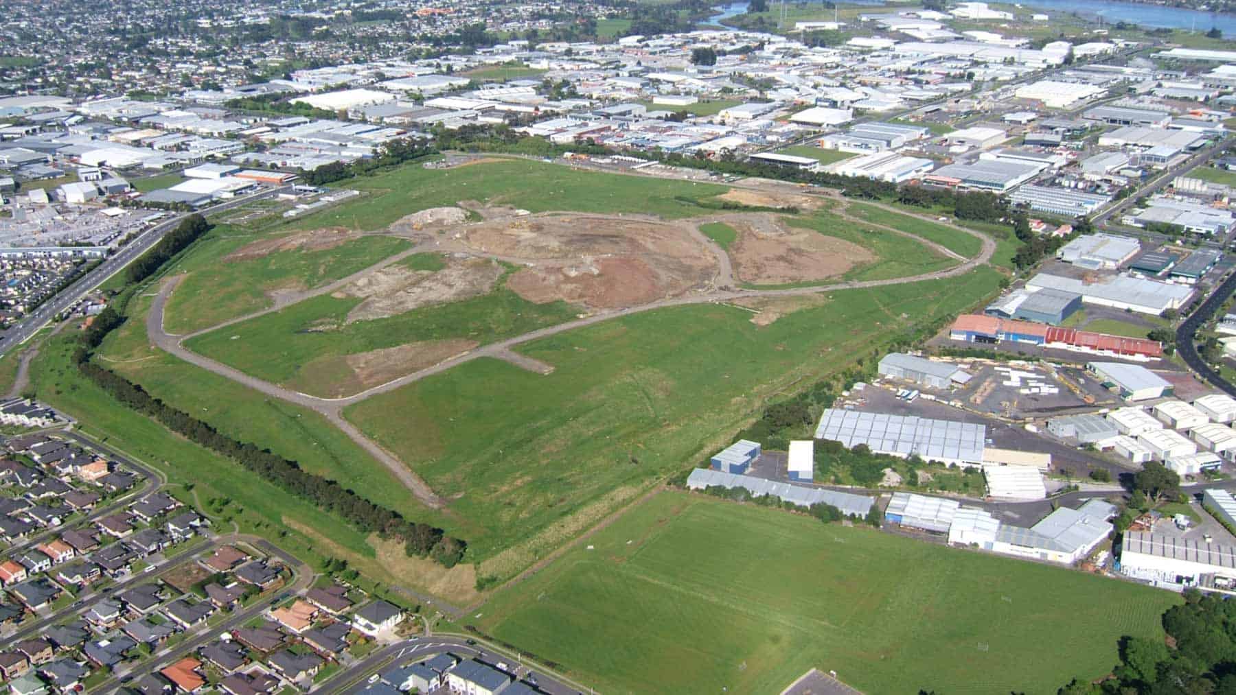Aerial view of the grass-covered former quarry and landfill at Matanginui / Green Mount, surrounded by industrial buildings and homes.