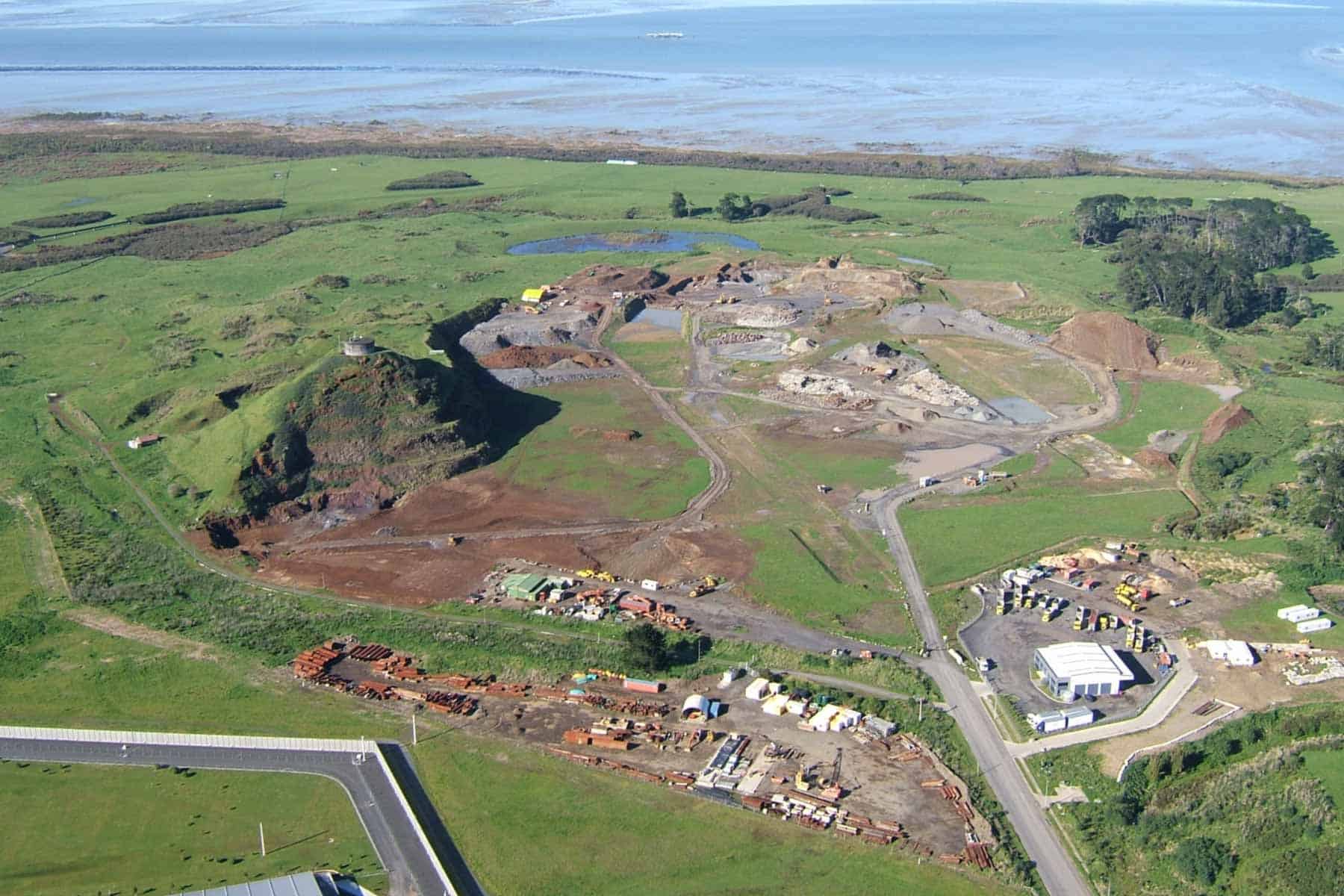 Aerial view of Matukutūreia / McLaughlins Mountain’s remaining volcanic cone and surrounding quarry, with grassy fields and the Manukau Harbour beyond.