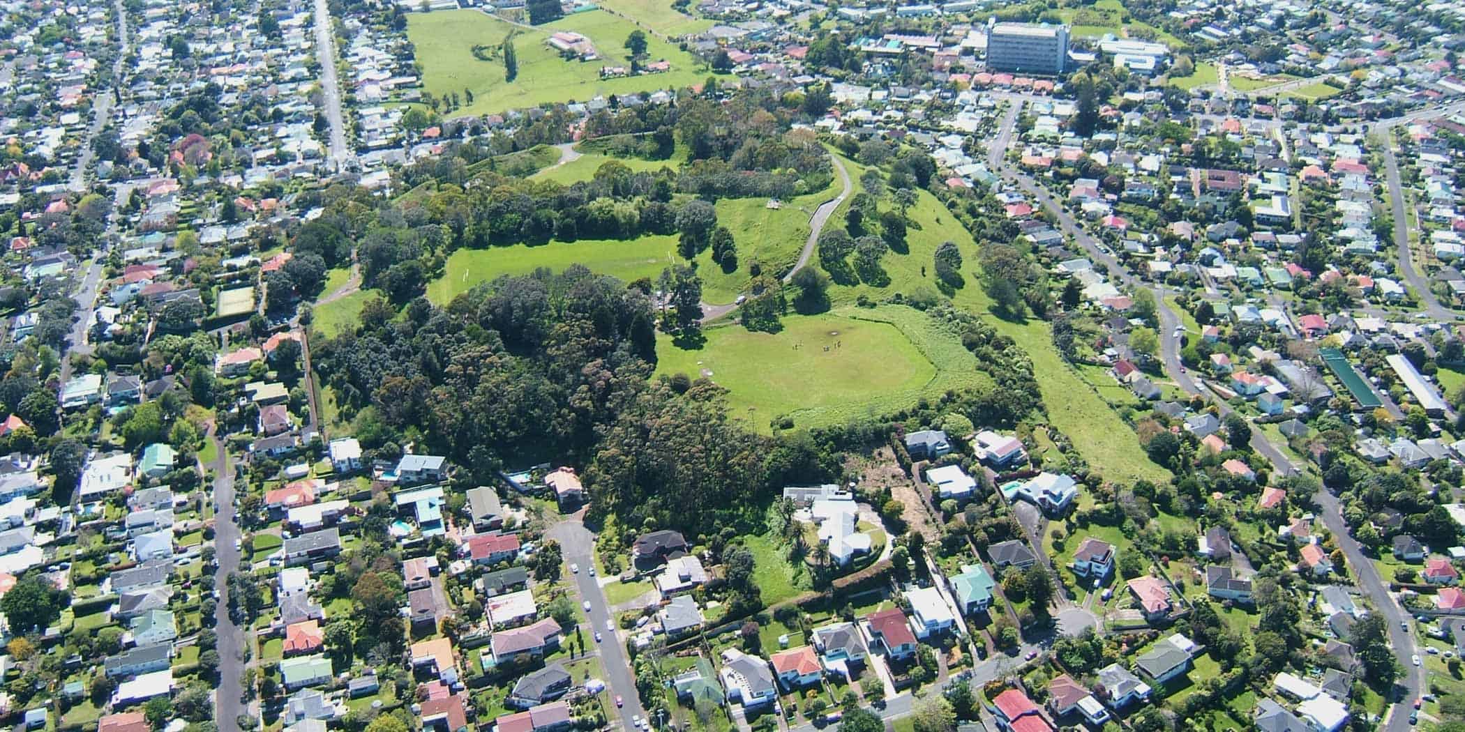 Aerial view of Ōwairaka / Mt Albert, showing its grassy volcanic cone, crater and surrounding Auckland suburbs.