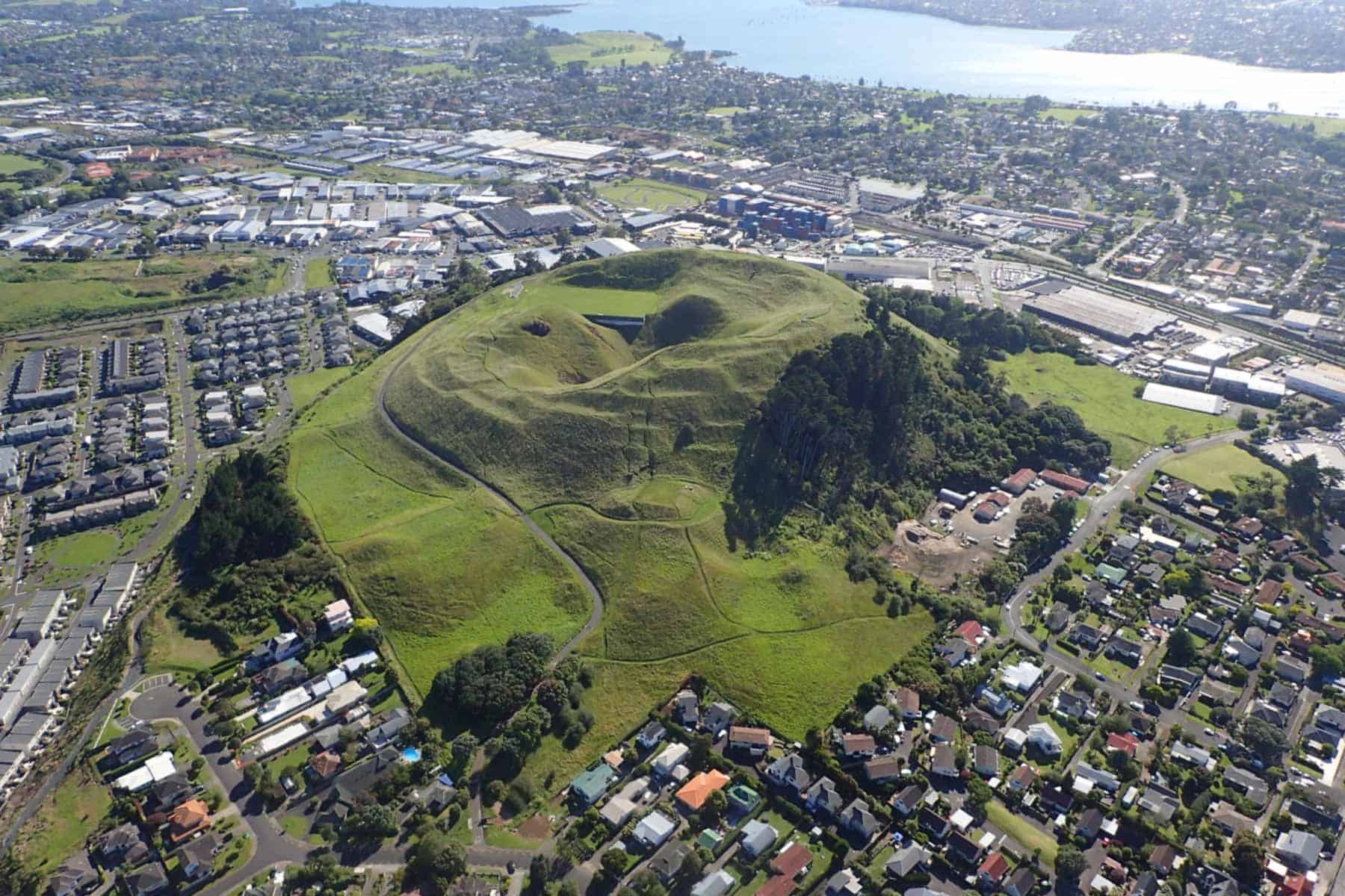 Aerial view of Maungarei / Mt Wellington, showing its grassy volcanic cone and summit craters surrounded by Auckland suburbs.