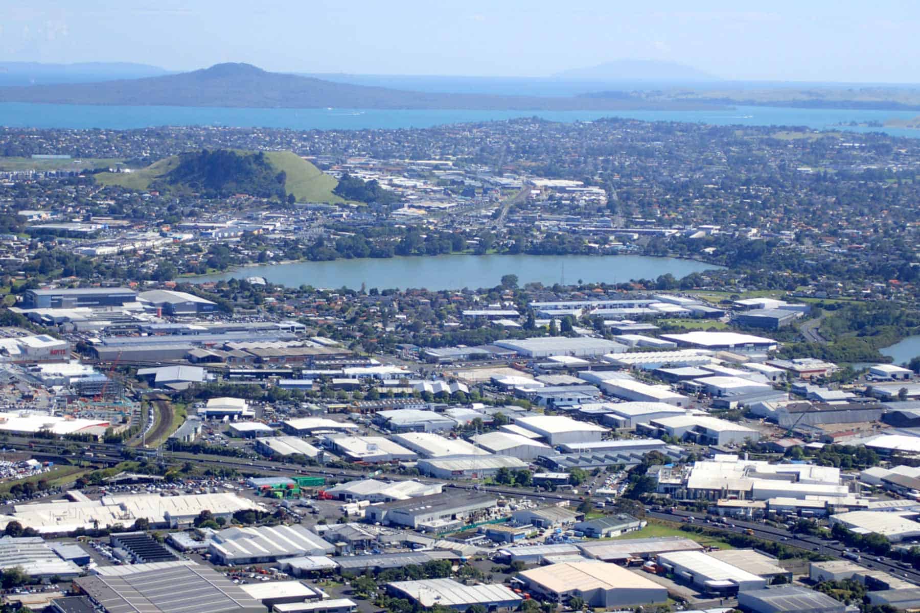 Aerial view of Te Kopua Kai-a-Hiku / Panmure Basin surrounded by Auckland suburbs and industrial buildings, with Maungarei and Rangitoto in the distance.