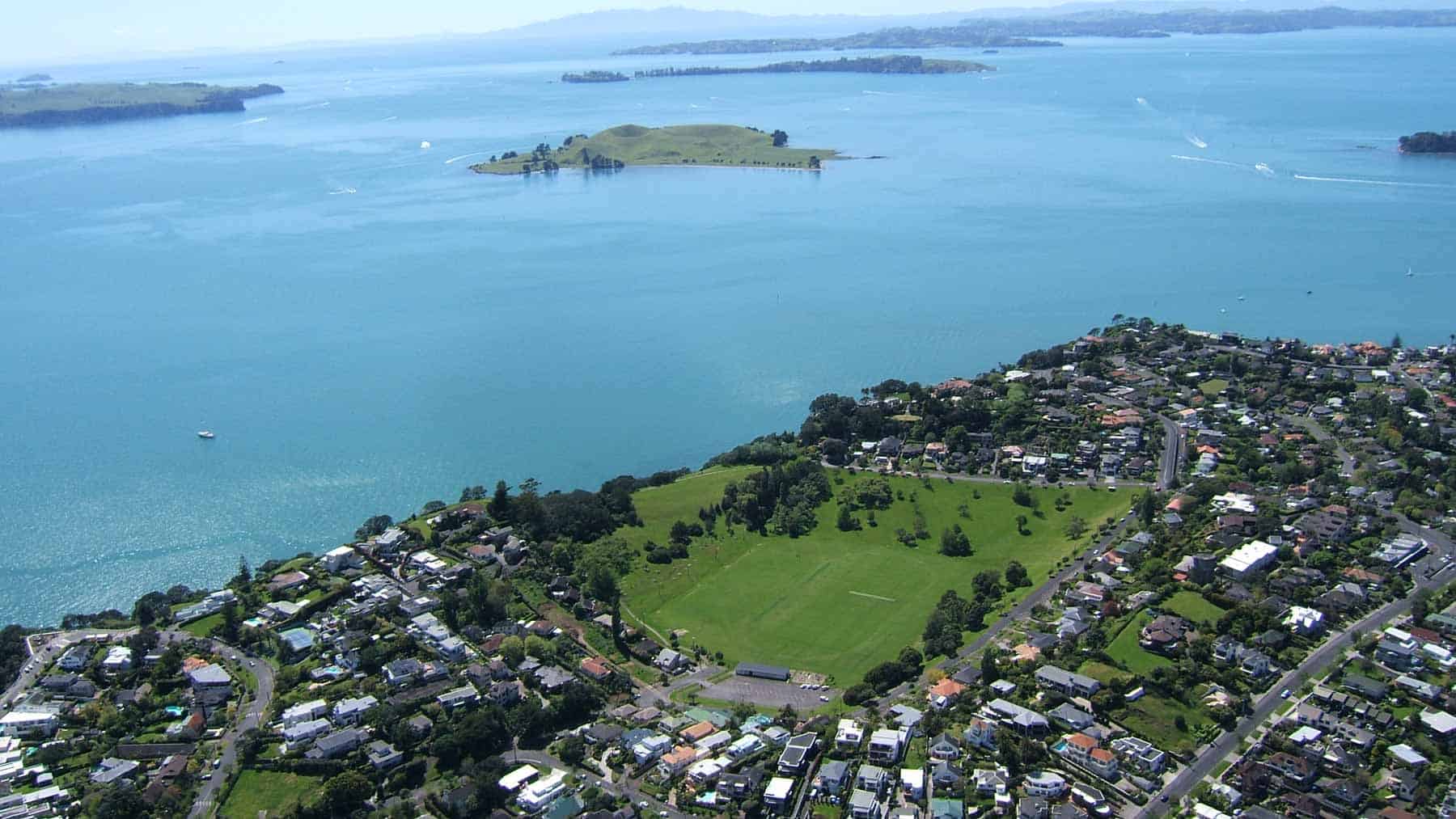 Aerial view of Whakamuhu / Glover Park in St Heliers, showing the grassy crater floor, surrounding homes and the Hauraki Gulf.