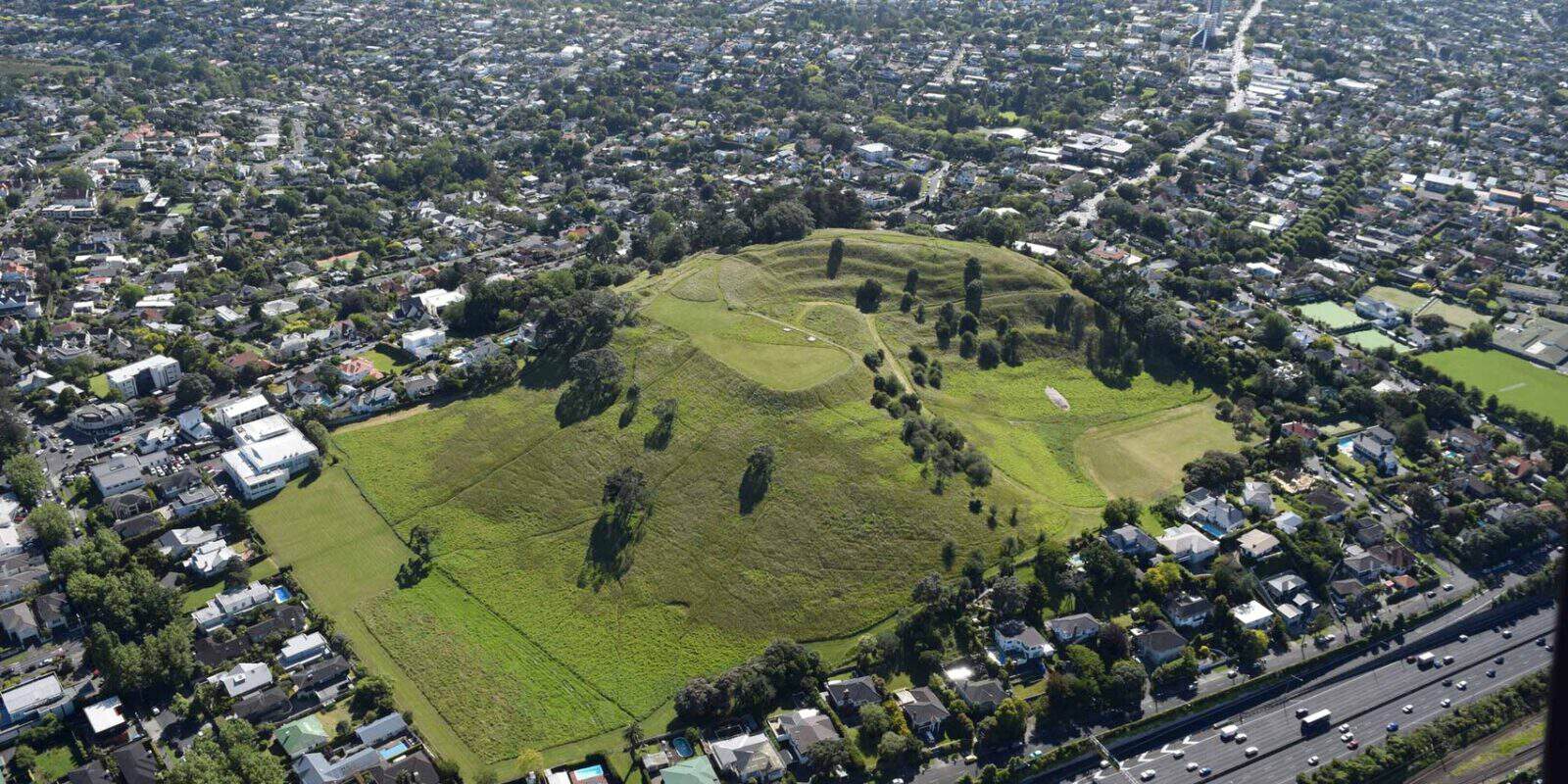 Aerial view of the grassed cone of Ōhinerangi / Mt Hobson beside the motorway