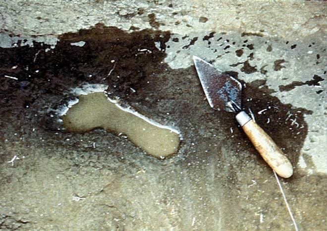 A human footprint pressed into the Rangitoto ash layer, with a trowel beside it for scale