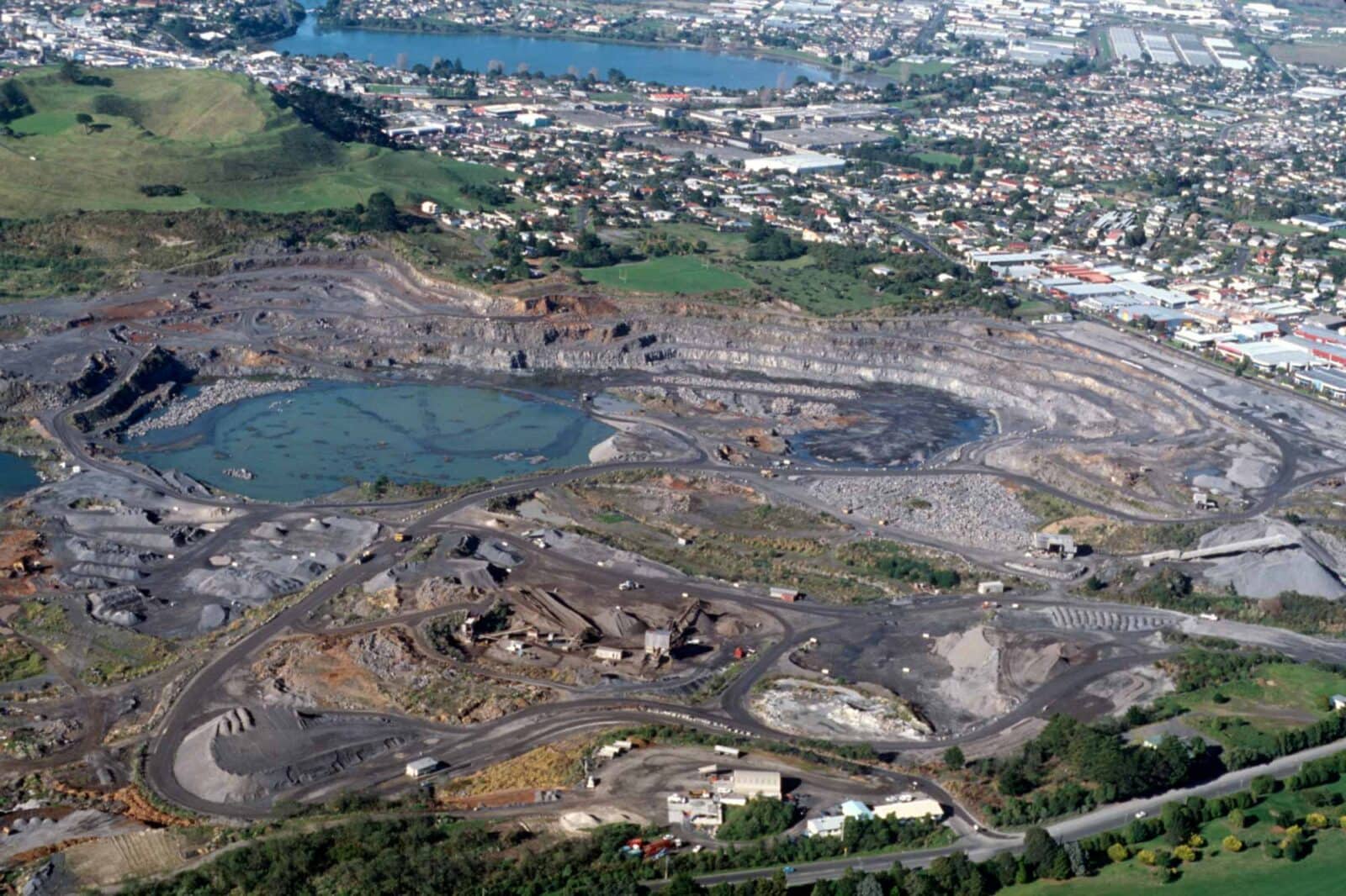 Aerial view of a volcano quarried down to a flooded pit, surrounded by industry and houses