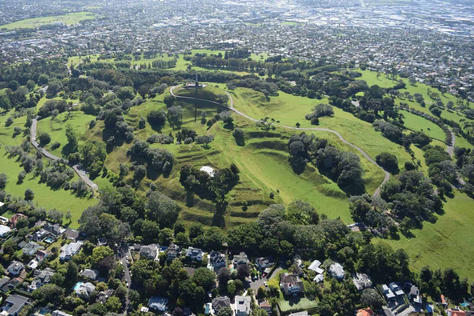 Aerial view of Maungakiekie / One Tree Hill, its terraced grassy cone and summit obelisk surrounded by suburbs