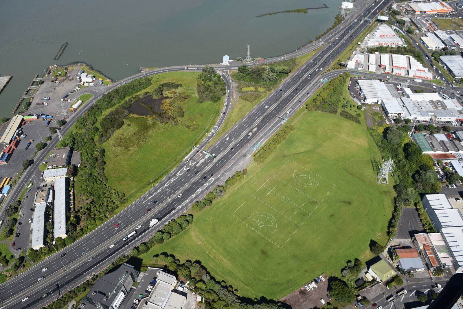 Aerial view of Te Hopua-a-Rangi / Gloucester Park, the green floor of a tuff ring cut through by the motorway beside the harbour