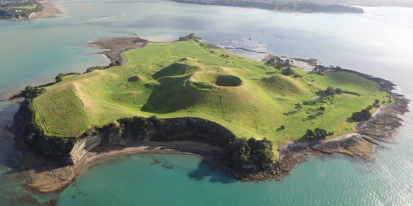 Aerial view of Motukorea / Browns Island: grassed scoria cones and a crater ringed by cliffs and the sea